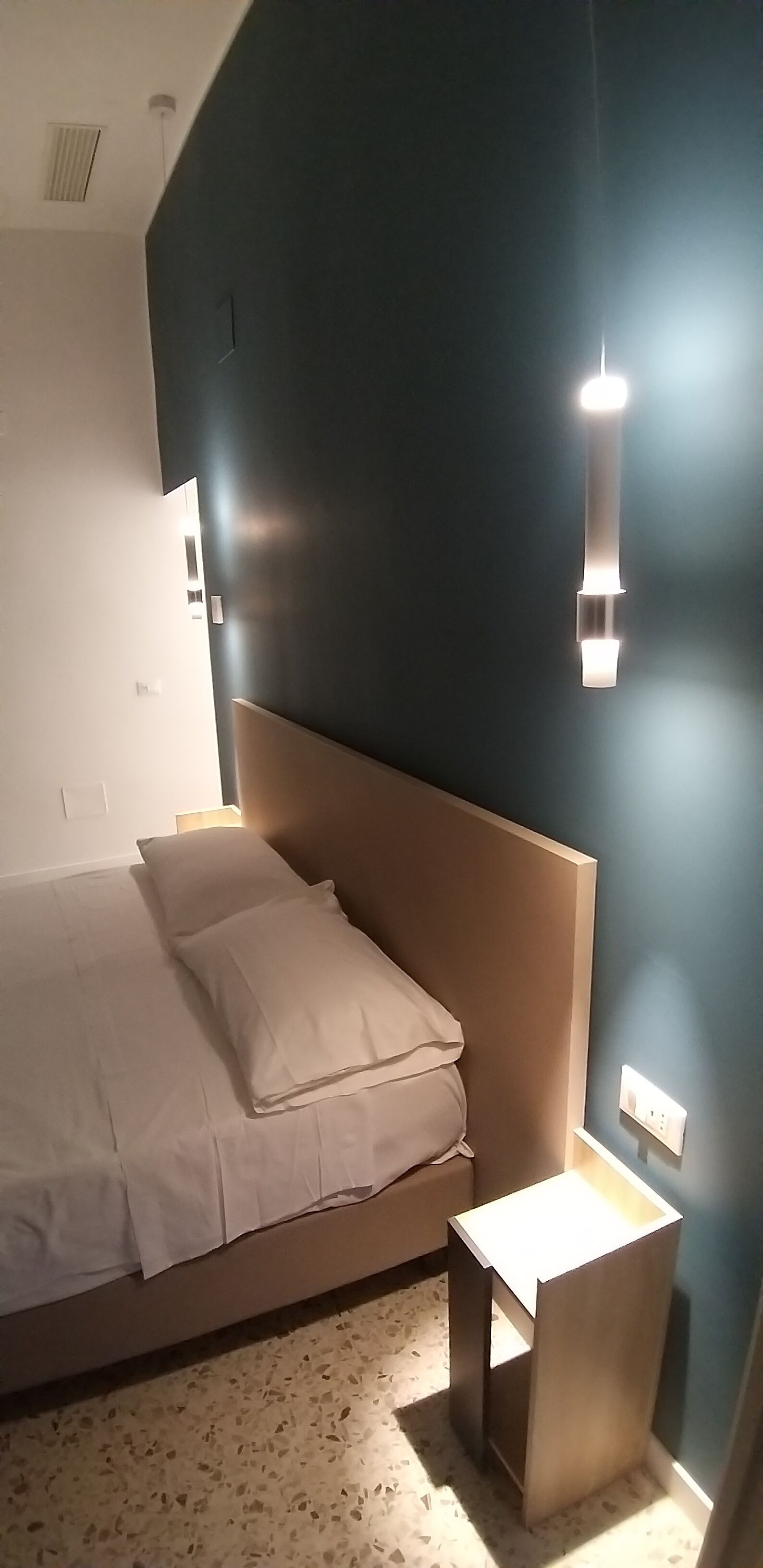 Een slaapkamer met een bed, nachtkastje en een wandlamp.