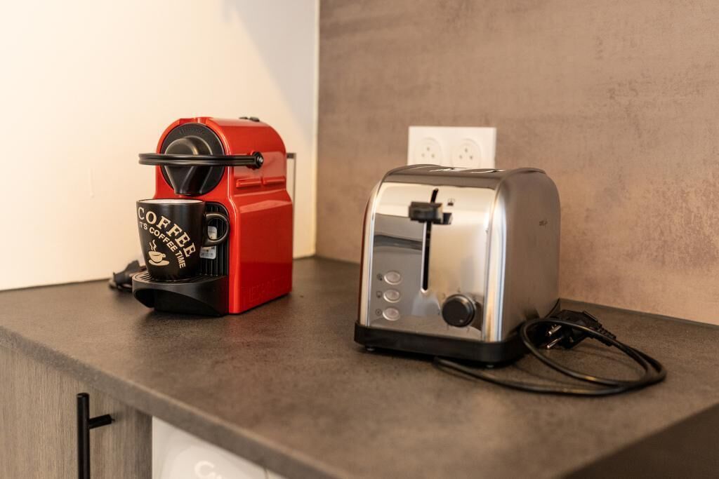 A red coffee maker and a silver toaster on a kitchen counter.