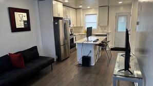 A modern kitchen with stainless steel appliances, a dining area with a glass table, and a black leather sofa with a red pillow. - Quaint 3/2.5 home in Fort Dupont (Washington)