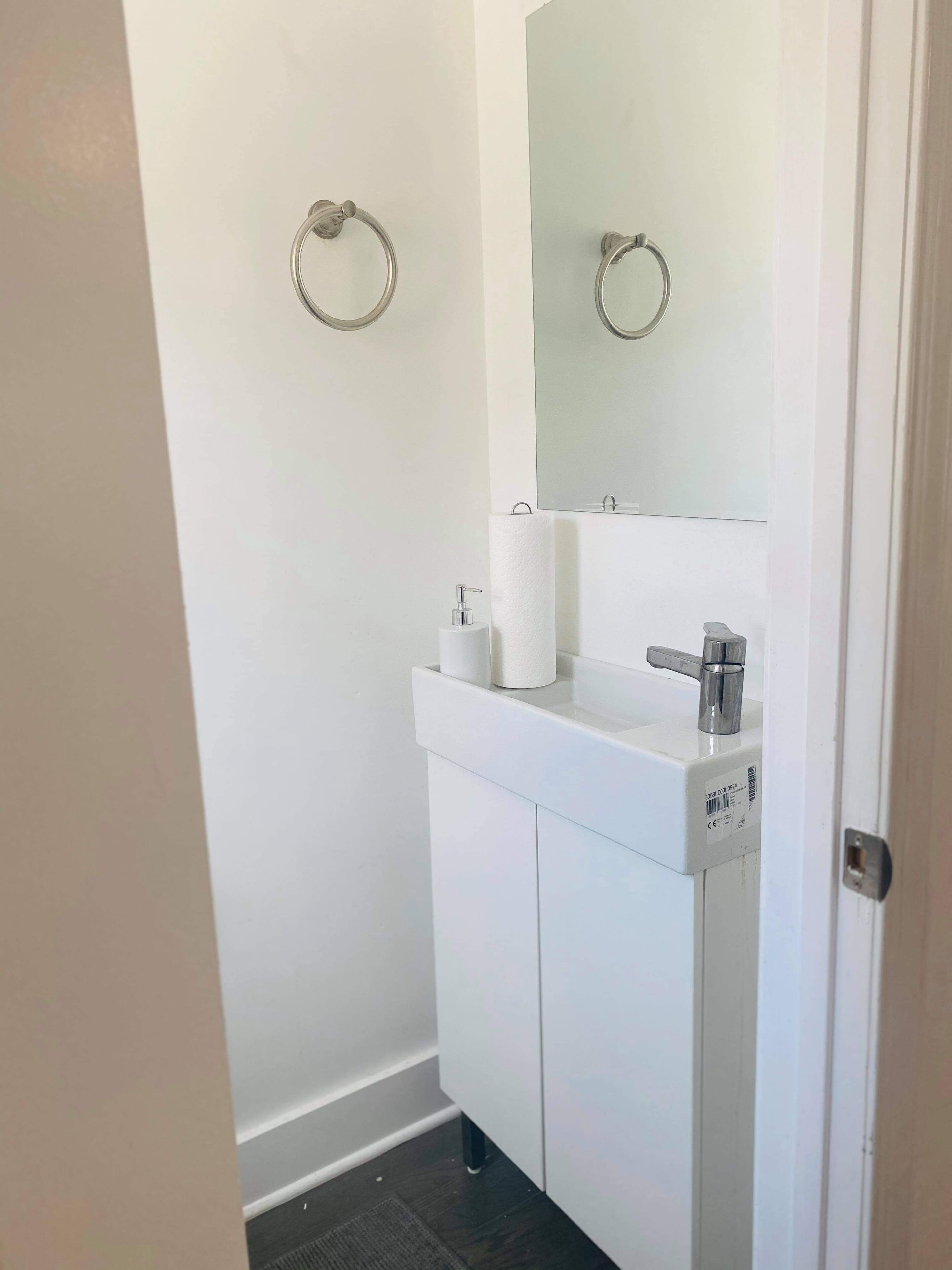 A small, white bathroom with a toilet paper holder, a mirror, and a sink.