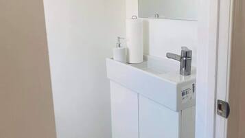 A small, white bathroom with a toilet paper holder, a mirror, and a sink.
