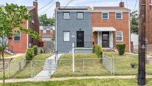 A two-story residential building with a grey facade, a black front door, and a small front yard with a fence. - Quaint 3/2.5 home in Fort Dupont (Washington)