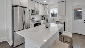 A modern kitchen with white cabinetry, stainless steel appliances, and a marble island. - Quaint 3/2.5 home in Fort Dupont (Washington)