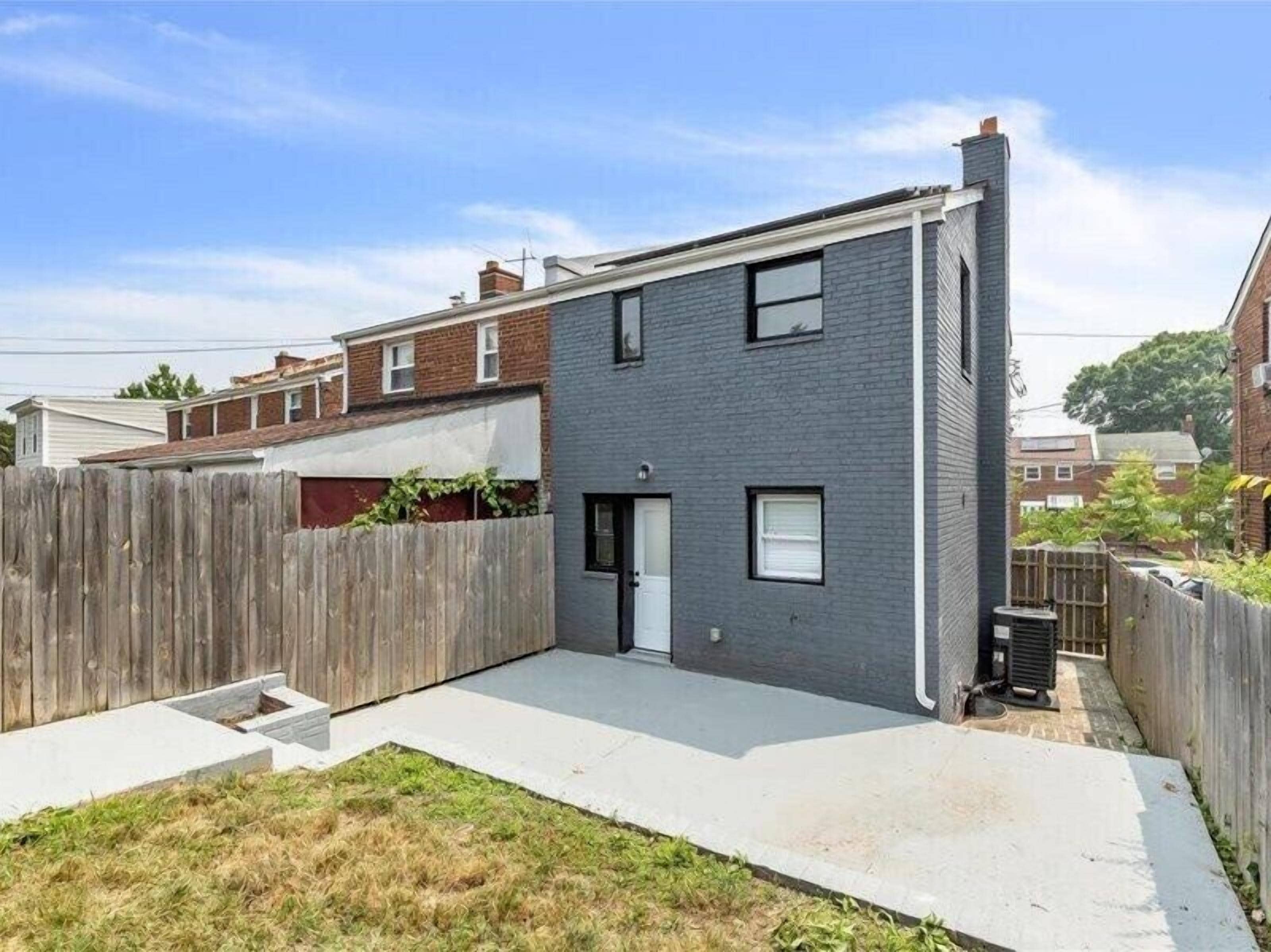 Una casa moderna de dos pisos con fachada gris, una puerta principal y un pequeño jardín delantero.