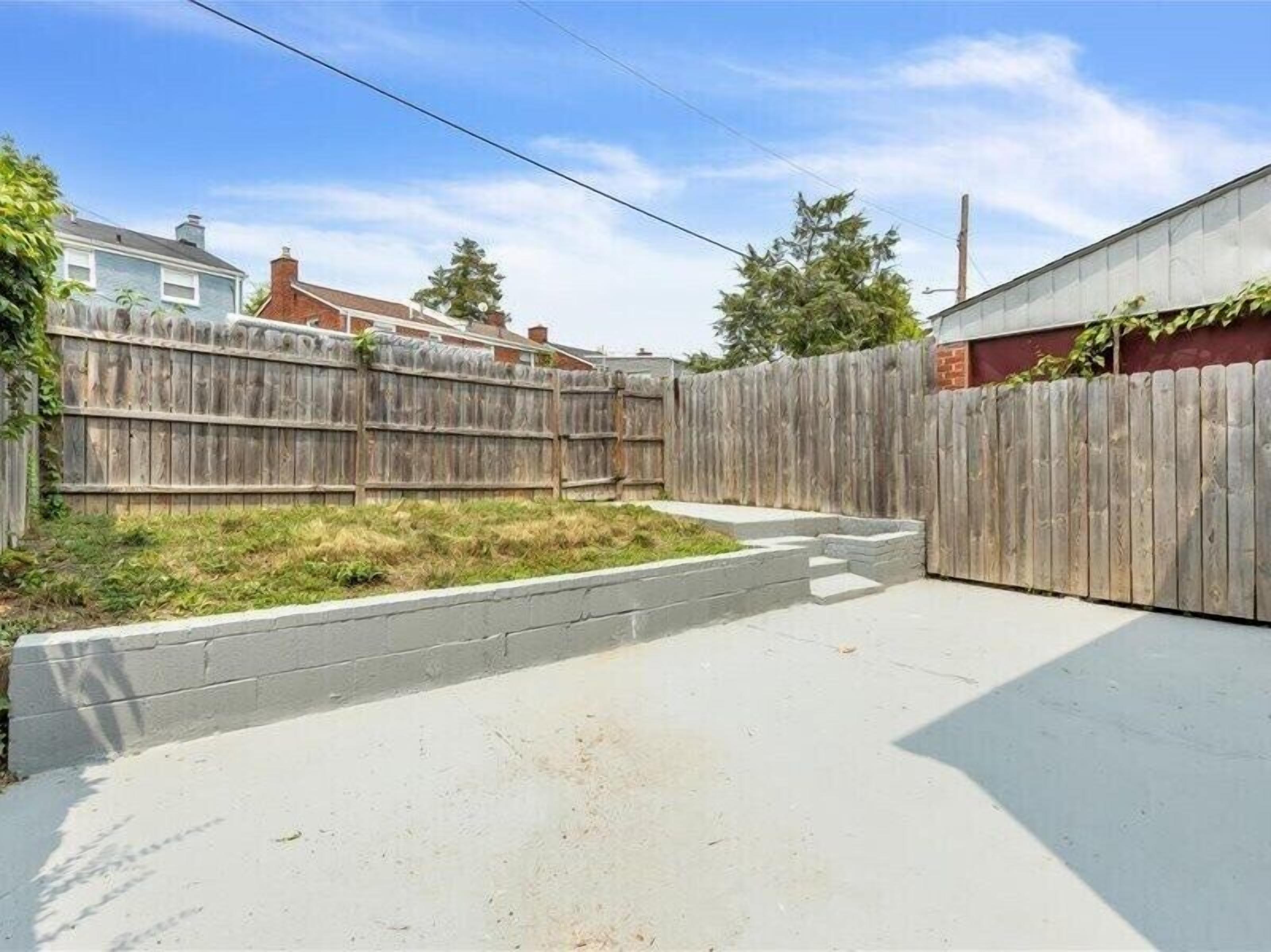 A backyard with a wooden fence, a concrete patio, and a grassy area.