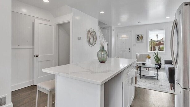A modern kitchen with white cabinetry, a marble island, and a stainless steel refrigerator. - Quaint 3/2.5 home in Fort Dupont (Washington)