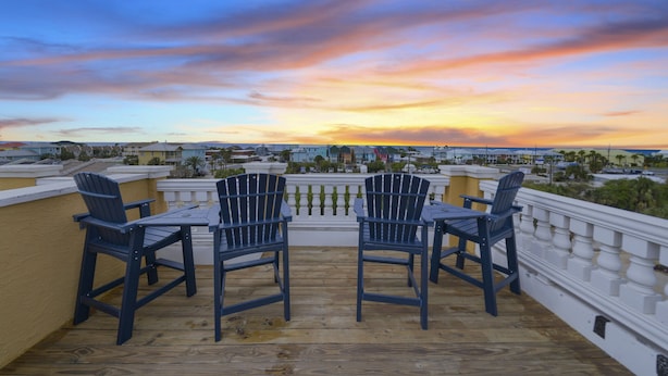 Um terraço com quatro cadeiras Adirondack e uma mesa, com vista para um horizonte urbano ao pôr do sol.