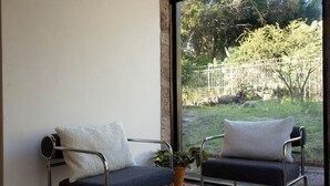 Una habitación moderna con dos sillas de metal, una mesita y un amplio ventanal con vistas a un jardín.