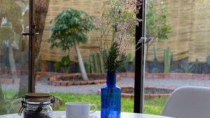 Una mesa con una taza de café, un jarrón azul con flores y un tarro de cristal con café.