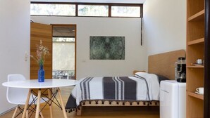 Habitación pequeña con cama, una mesita, una silla, cafetera y un cuadro en la pared.