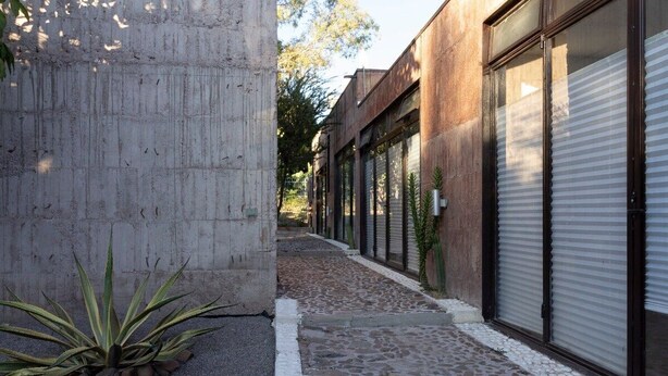 Un callejón estrecho con un muro de hormigón a un lado y un edificio con grandes ventanales al otro.