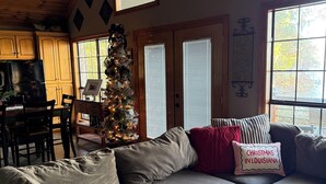 Un salon chaleureux avec un canapé gris, un sapin de Noël et une fenêtre avec des stores.