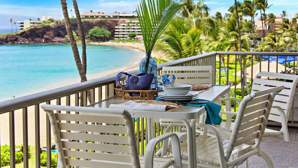 Ein Balkon mit Tisch für zwei Personen, Blick auf einen Strand mit Palmen und einem wolkenlosen, blauen Himmel.