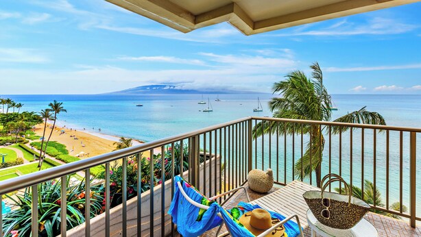 A balcony with a view of a beach, palm trees, and boats on the water. - Ocean Frnt steps from beach, dining, shopping 801 (Lahaina)