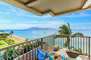Un balcon avec vue sur une plage, des palmiers et des bateaux sur l’eau.