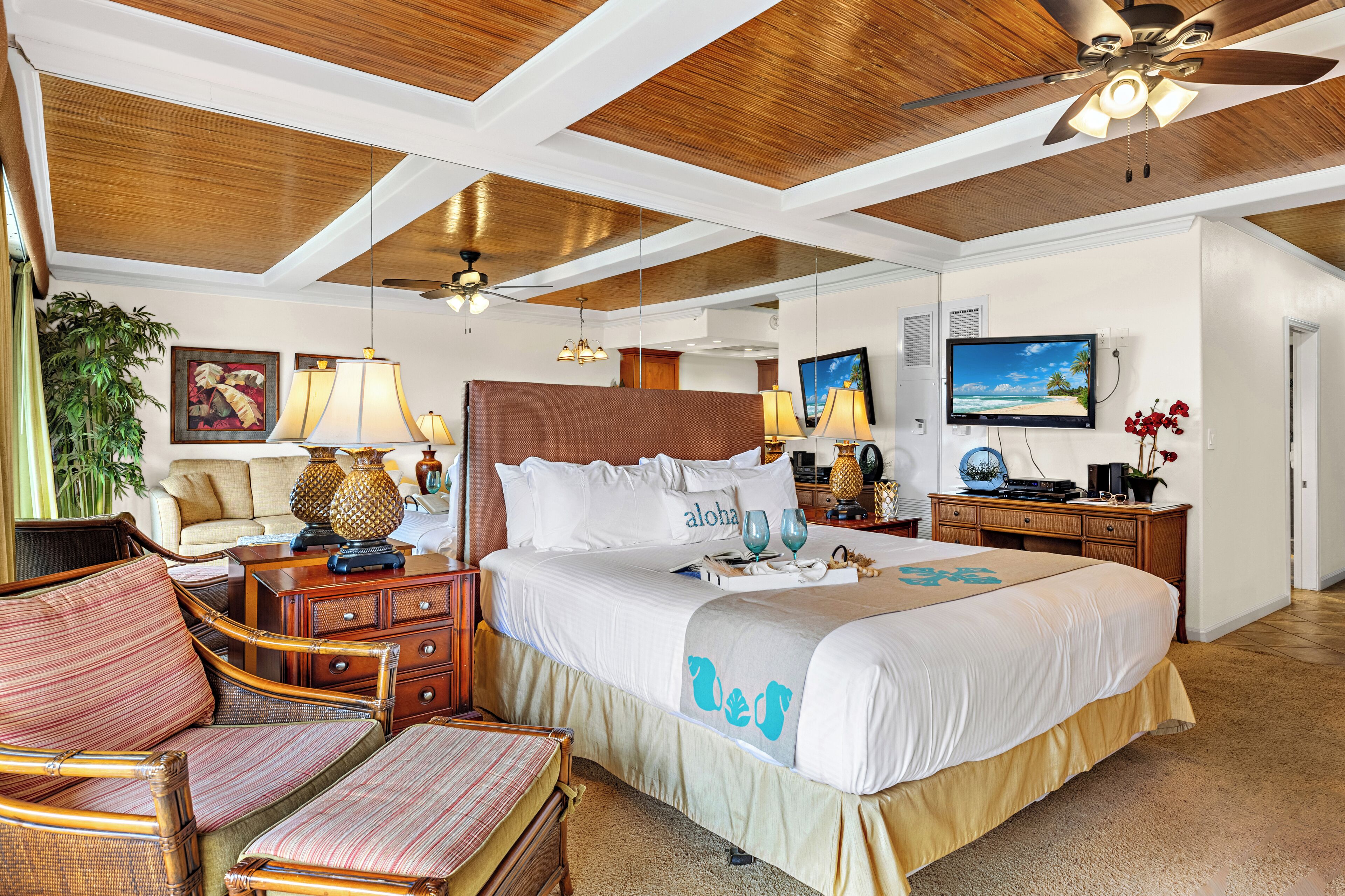 A spacious bedroom with a large bed, wooden ceiling, and a television on the wall.