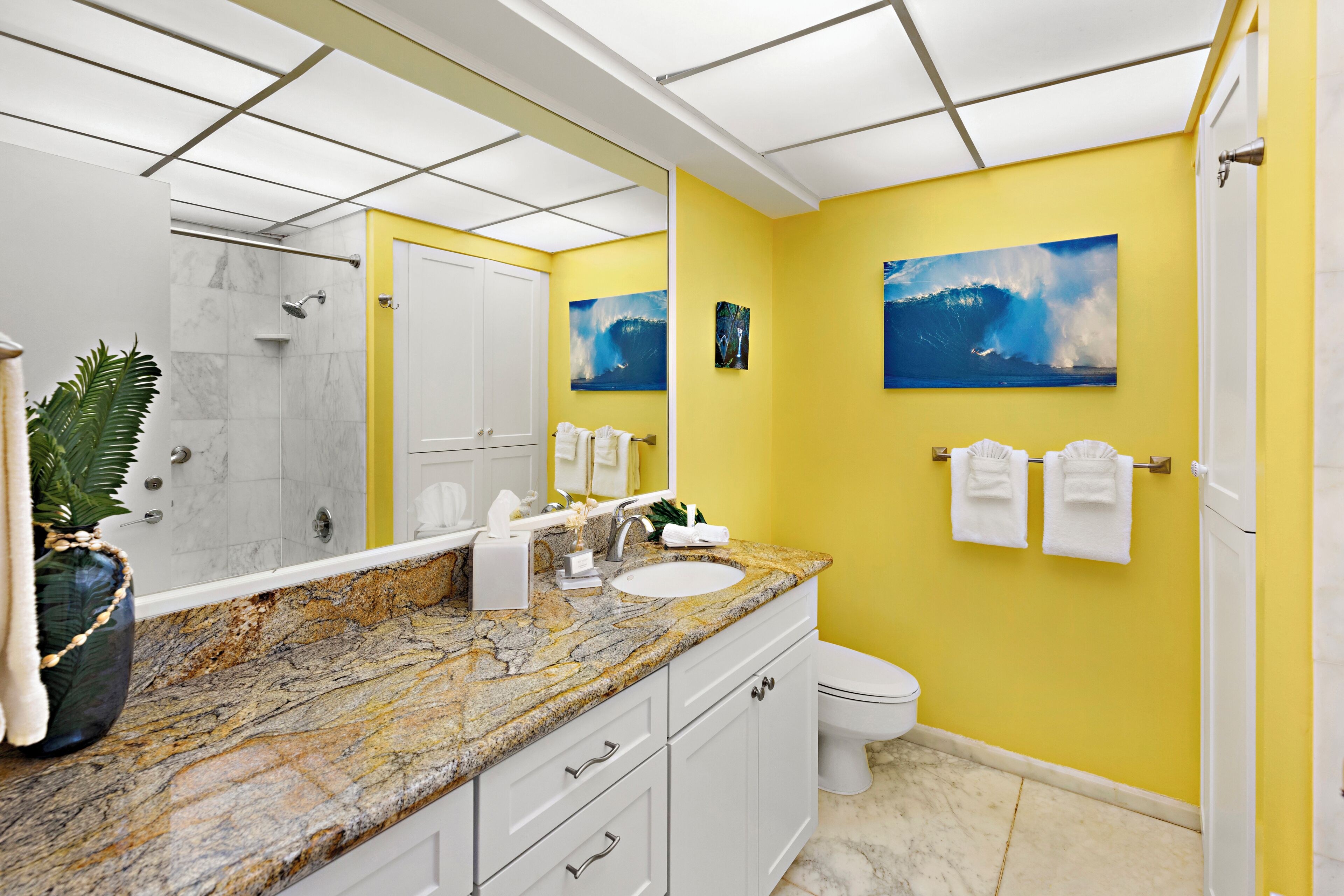Een badkamer met een gele wand, een wit toilet, een wastafel en een douchehoek.