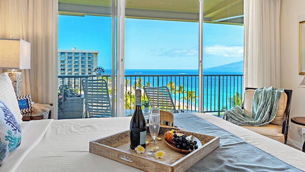 Une chambre d'hôtel avec balcon, un lit avec un plateau de nourriture et de boissons, et une vue sur l'océan.