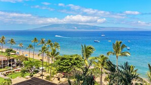 A tropical beach with clear blue water, palm trees, and boats. - Ocean View steps from beach, dining, shopping 961 (Lahaina)
