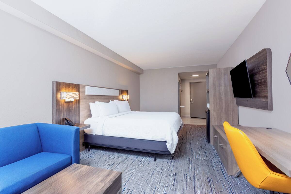 Una habitación de hotel moderna con una cama grande, un sofá azul, un escritorio de madera y una silla amarilla.