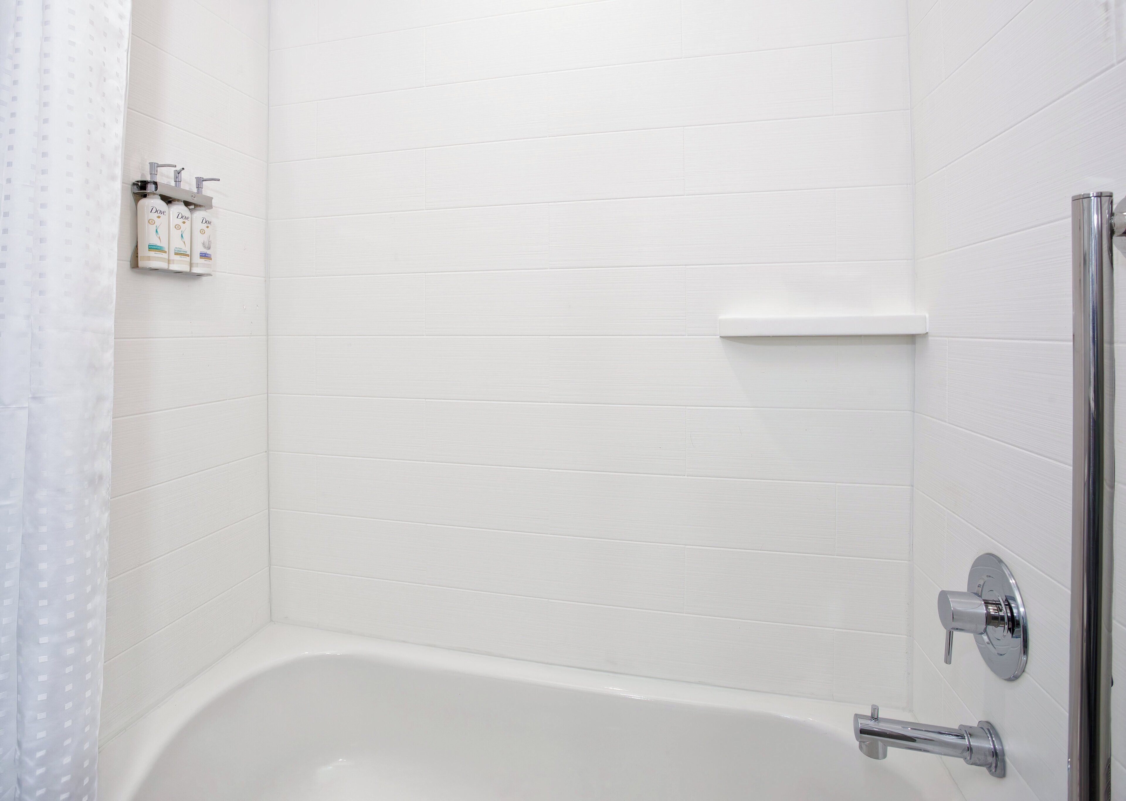 Un baño con una bañera blanca, ducha y estante con artículos de aseo.