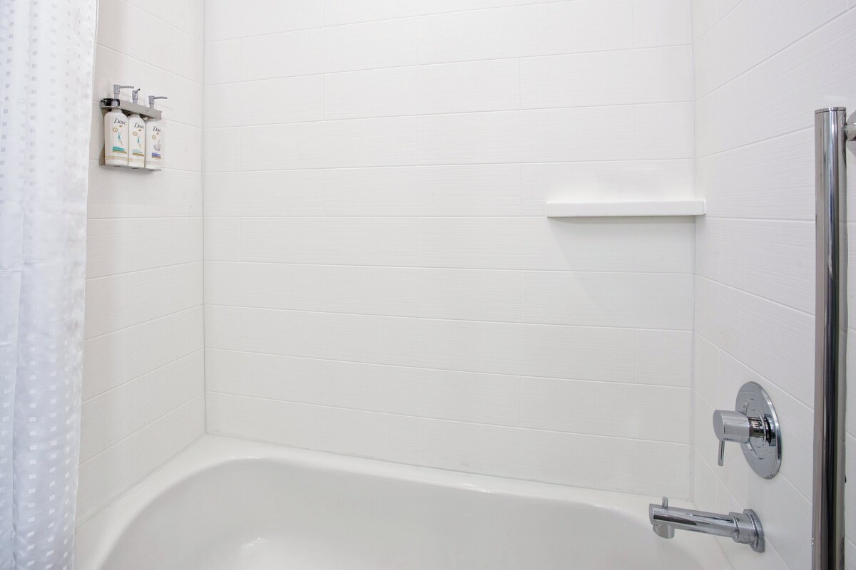 Un baño con una bañera blanca, ducha y estante con artículos de aseo.