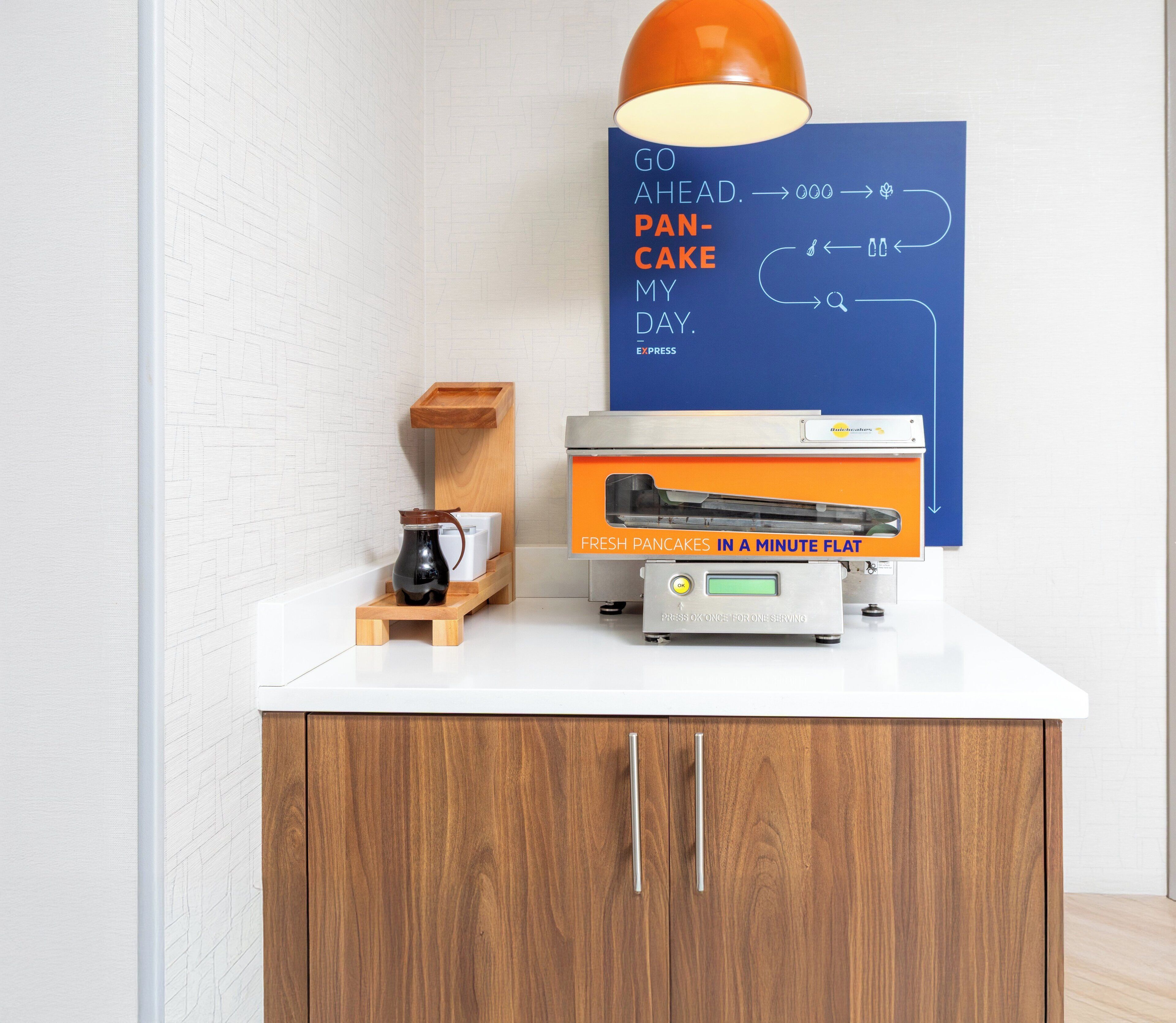 A kitchen counter with a coffee maker, a flat-screen TV, and a sign advertising fresh pancakes.
