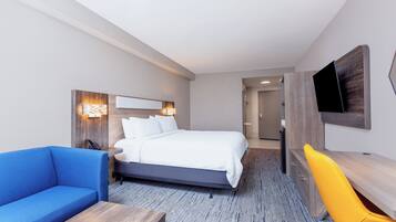 A modern hotel room with a large bed, a blue sofa, a wooden desk, and a yellow chair.