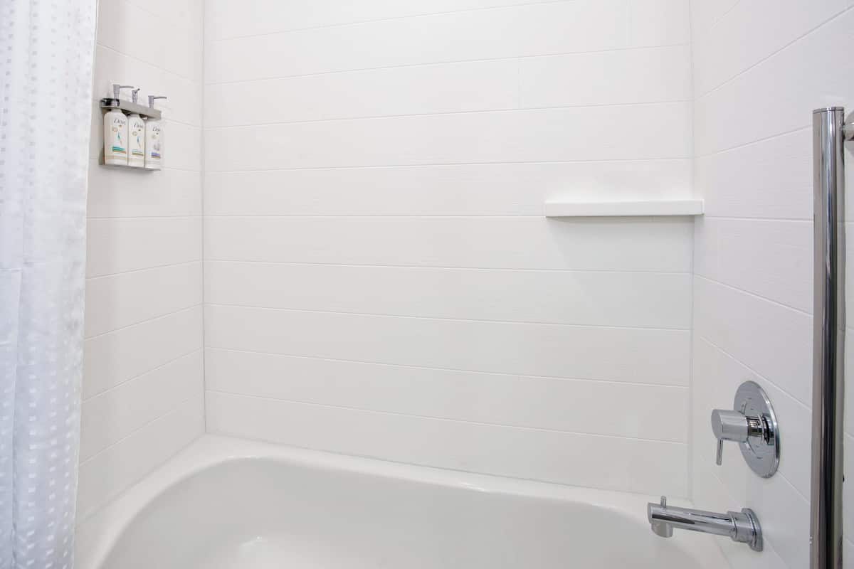 Un baño con una bañera blanca, ducha y estante con artículos de aseo.