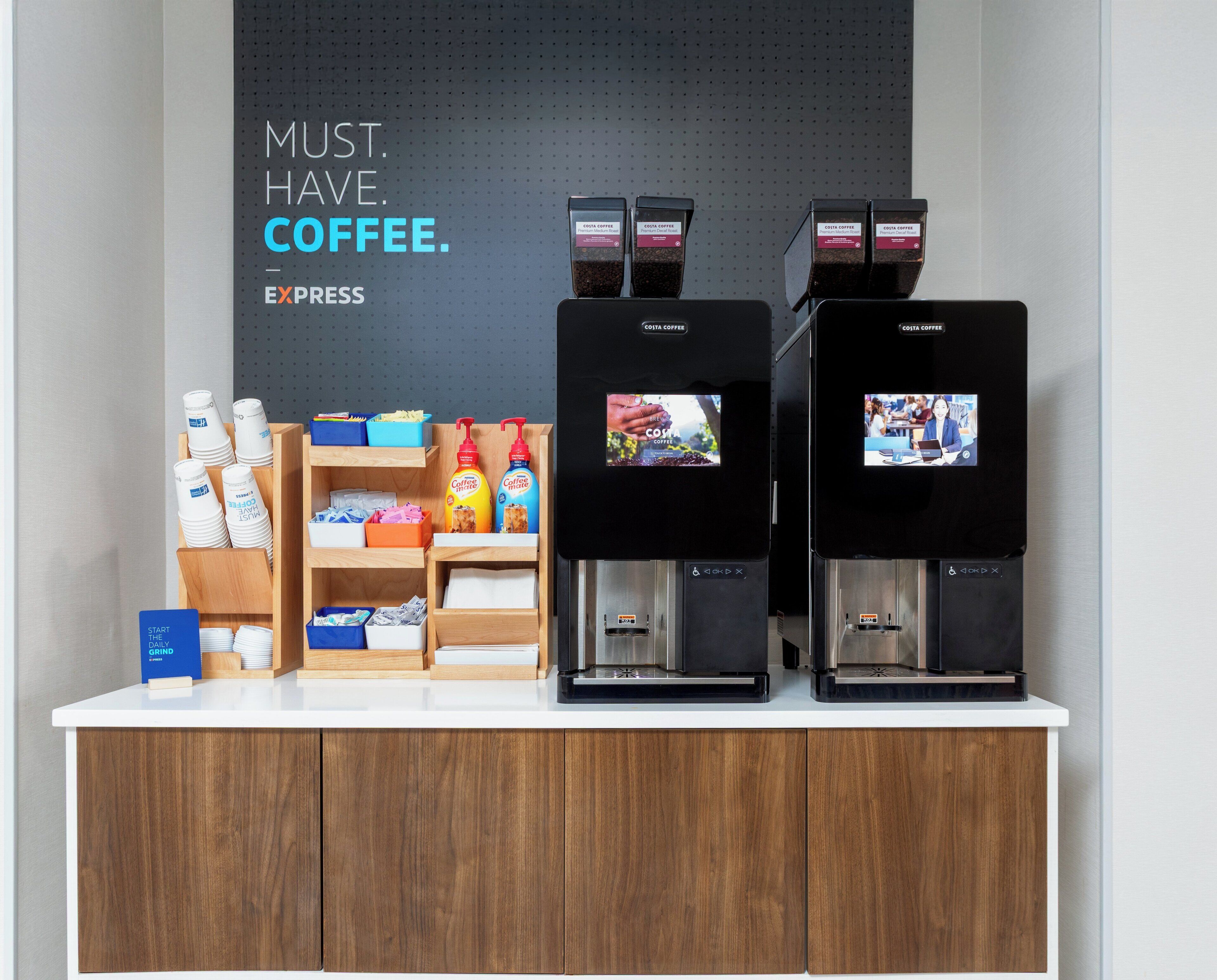 A coffee station with two espresso machines, coffee pods, and a sign that reads "MUST HAVE COFFEE."