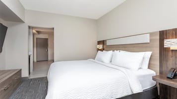 Una habitación de hotel moderna con una cama grande, cabecera de madera, mesita de noche con lámpara y vistas al pasillo.