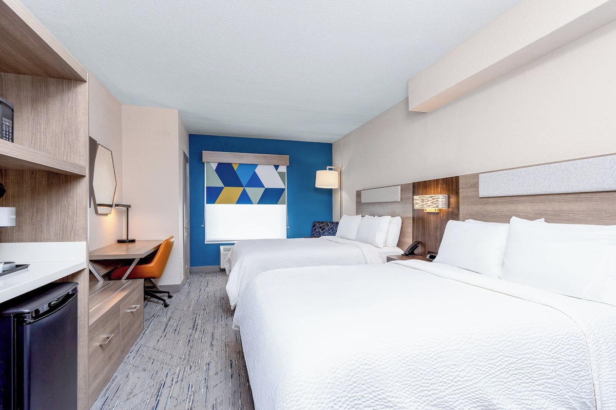 Habitación de hotel con dos camas, un escritorio con silla, un refrigerador pequeño y una pared de acento azul.