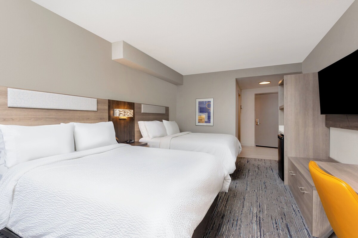 Habitación de hotel con dos camas, un escritorio, una silla, un televisor y un baño a la vista.
