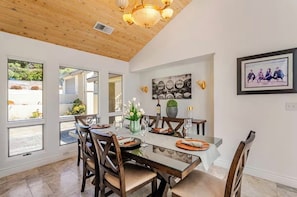 Un comedor con techo de madera, ventanas amplias y una mesa preparada para cuatro comensales.
