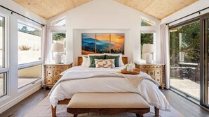 Een slaapkamer met een groot bed, een schilderij erboven en een uitzicht op het landschap door grote ramen.