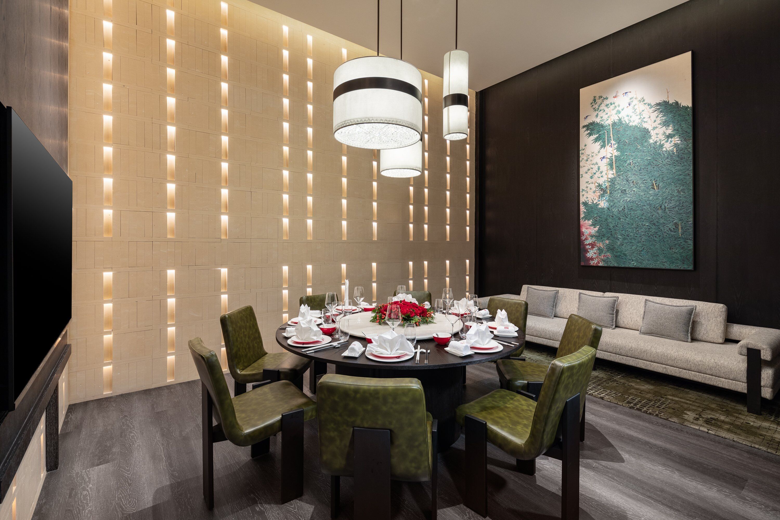 A modern dining area with a round table set for six, surrounded by green upholstered chairs.