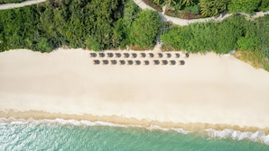 Vista aérea de uma praia com fileiras de espreguiçadeiras e uma visão ampla do oceano.