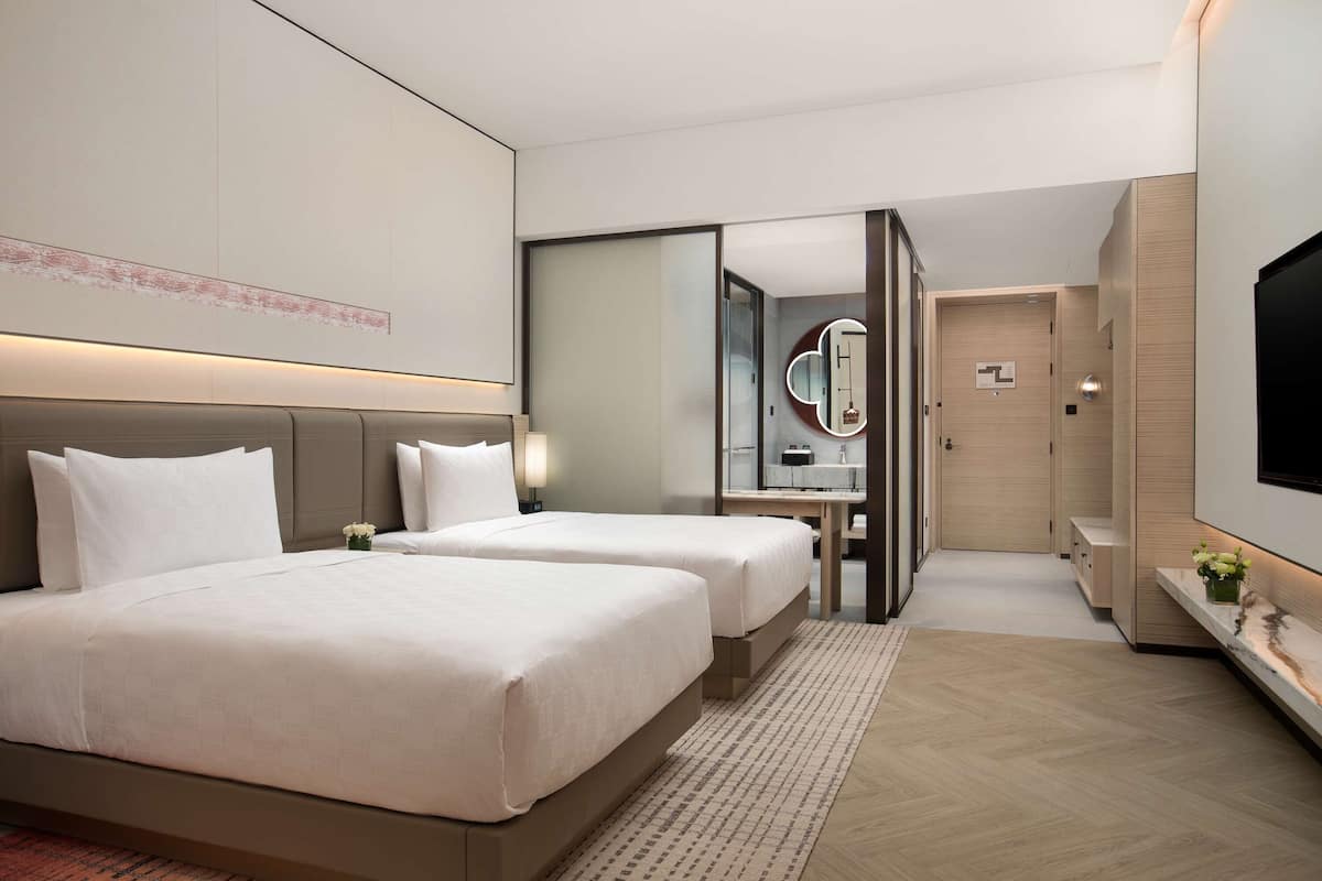 A hotel room with two beds, a large mirror, a TV, and a small table with a vase of flowers.