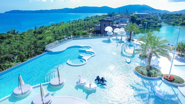 Piscina de resort com efeito de onda, rodeada por palmeiras e vista para o mar.