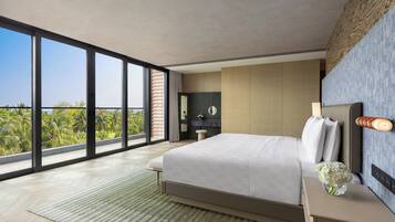 A modern bedroom with a large bed, a nightstand, a mirror, and a view of palm trees through large windows.