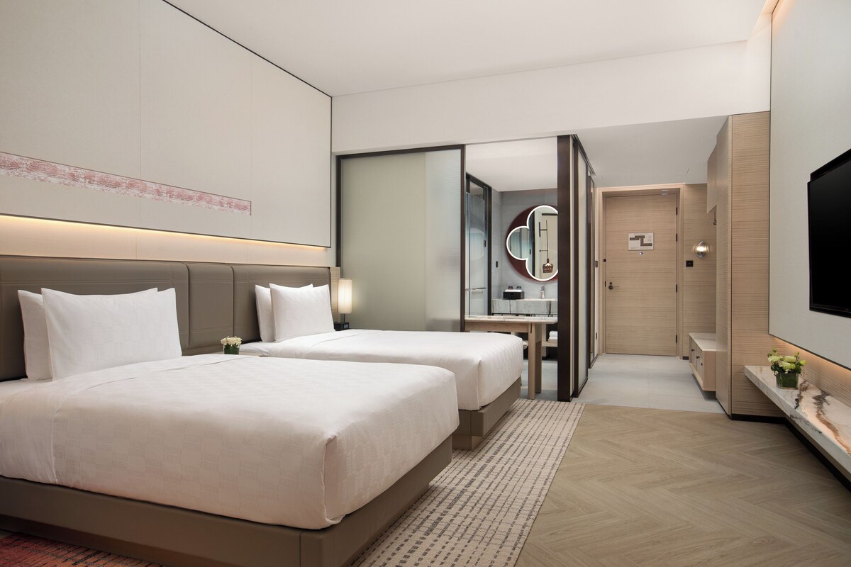 Une chambre d’hôtel avec deux lits, un grand miroir, une télévision et un plancher en bois.