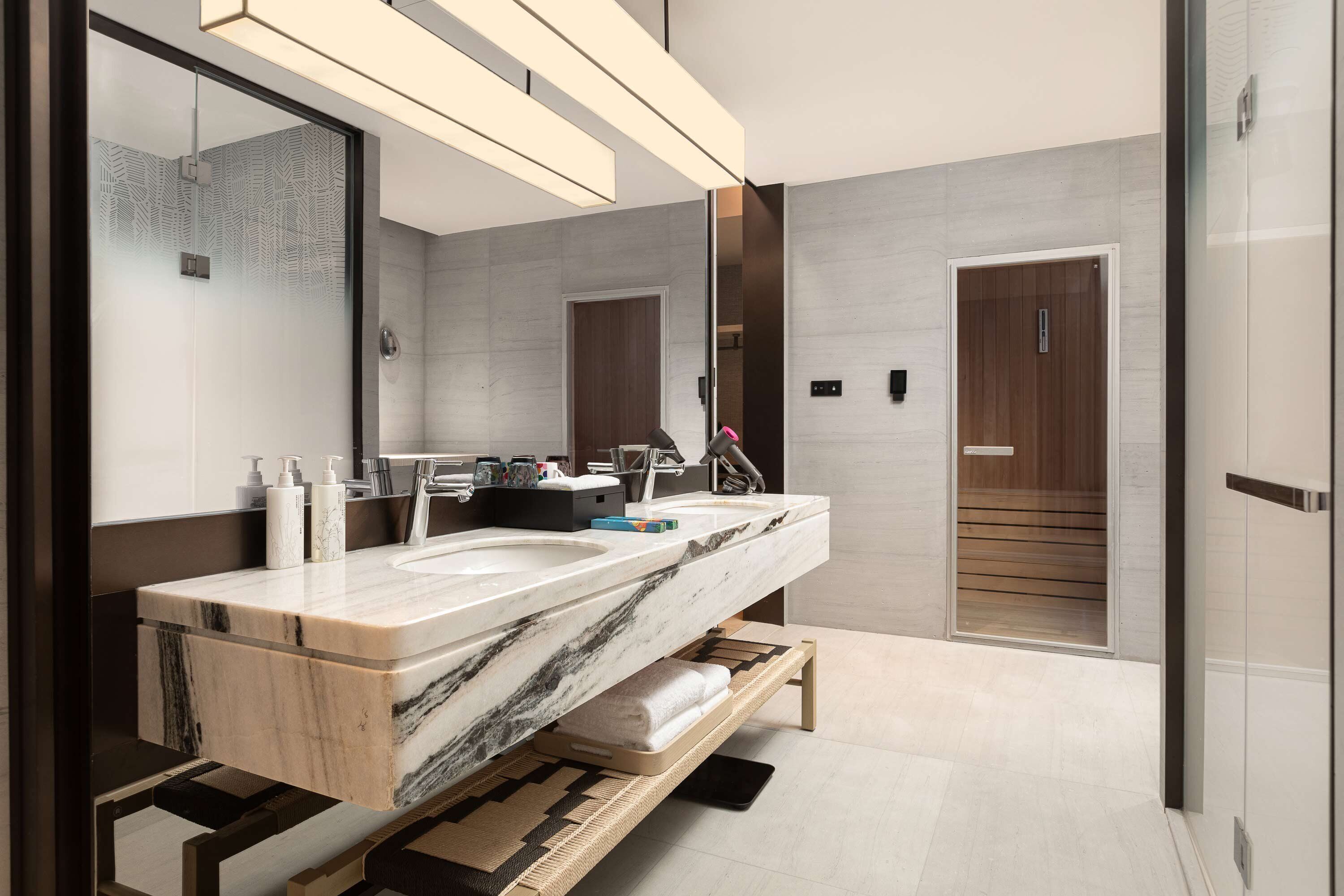 Un baño moderno con un lavamanos grande de mármol, un espejo y una puerta de madera.