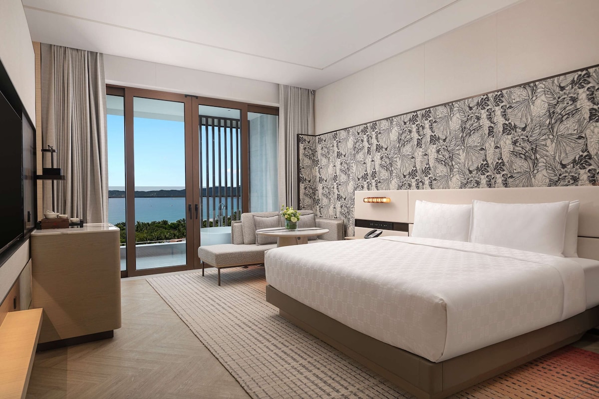 A modern hotel room with a large bed, a seating area with a view, and a balcony with a scenic view.
