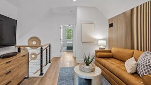 A modern living room with a wooden sofa, a TV, and a staircase leading to another room.