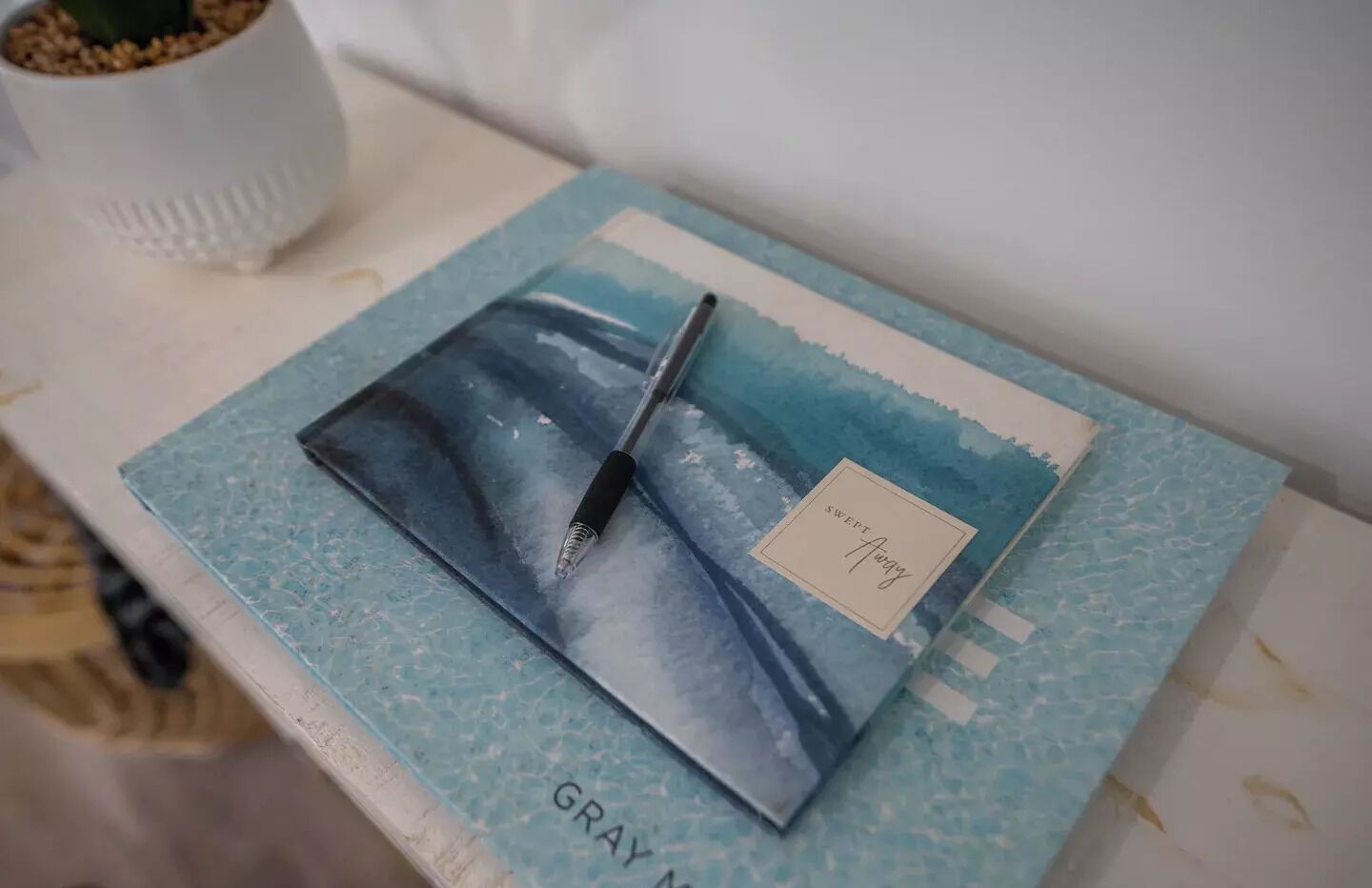 Een notitieboekje met een blauwe omslag en een pen erboven, op een witte ondergrond.