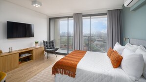 A modern hotel room with a large bed, a flat-screen TV, a desk with a chair, and a view of the city through large windows. - Parque Jockey Pinheiros (São Paulo)