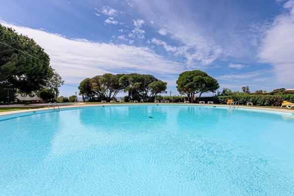 A clear blue pool with lounge chairs and trees in the background.