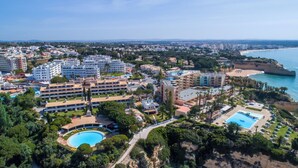 Vista aérea de un complejo turístico costero con varios edificios hoteleros, una piscina central y una zona de playa.
