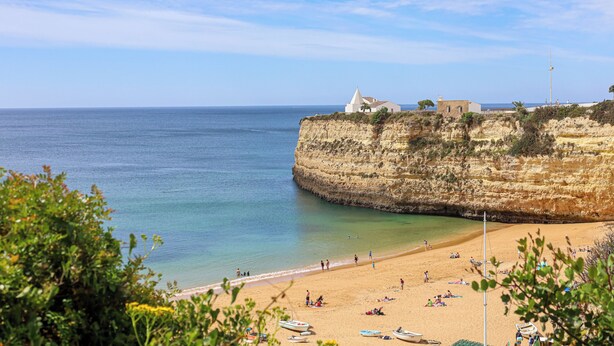 Una playa costera con un acantilado, un faro y algunas embarcaciones.