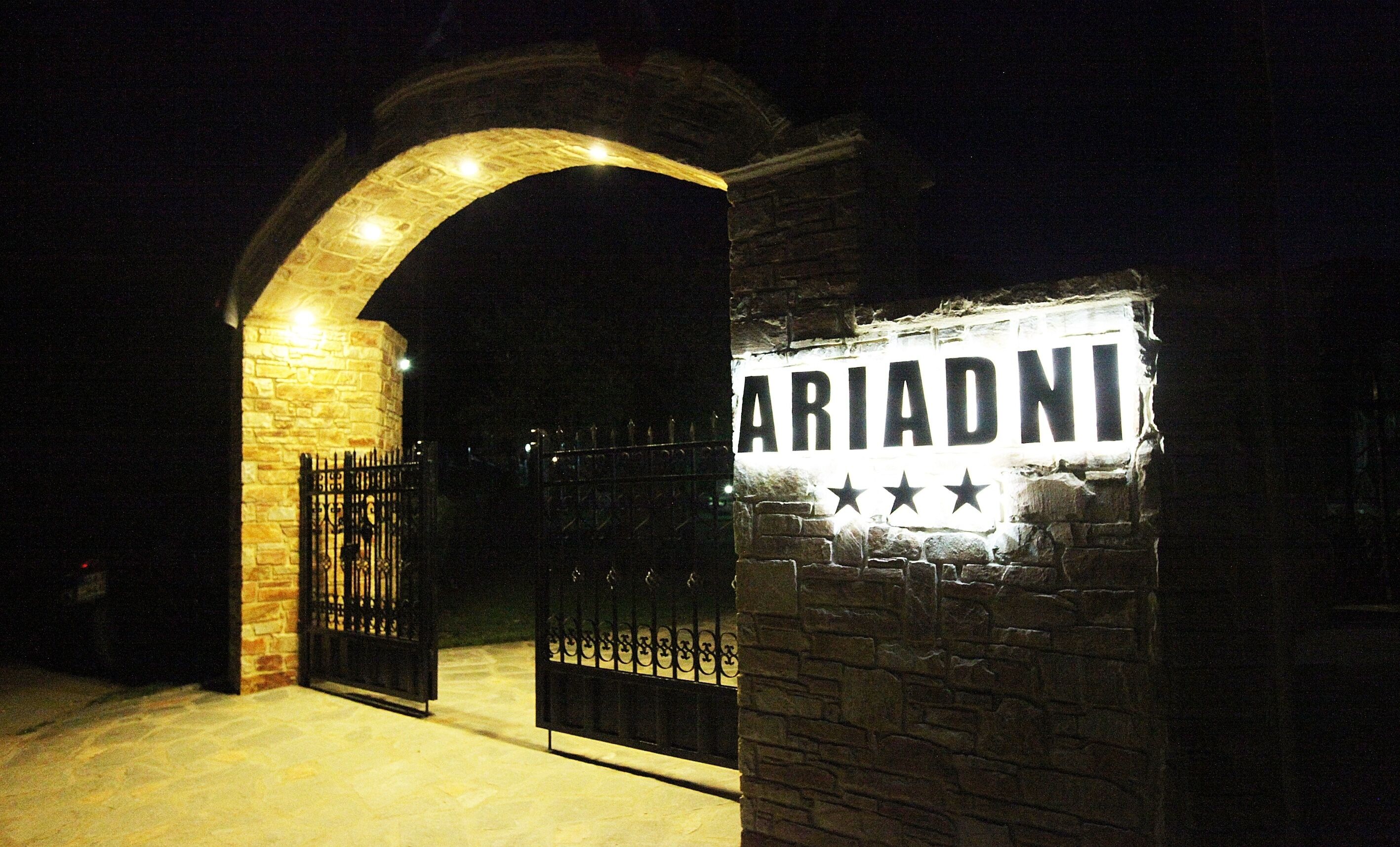 A stone archway leading to a gated entrance with a sign that reads "ARIADNI".